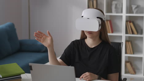 Frau-Trägt-Ein-Head-Mounted-Display-Zur-Betrachtung-Virtueller-Realität,-Sitzt-Zu-Hause-Und-Gestikuliert-Mit-Der-Hand-über-Den-Bildschirm